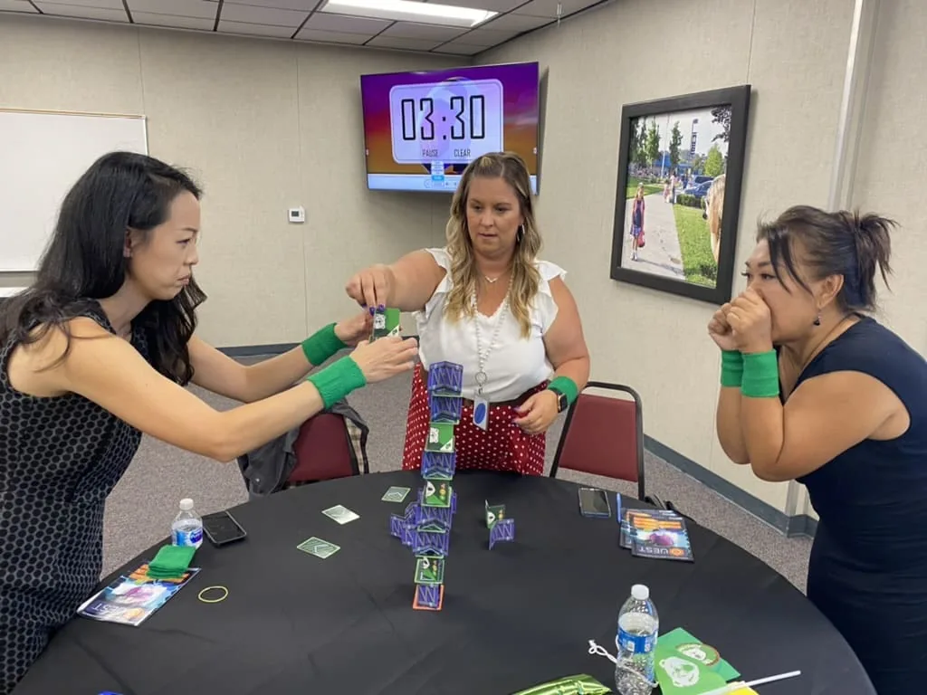 Three educators race to build a card tower as the countdown timer on screen reads 3:30
